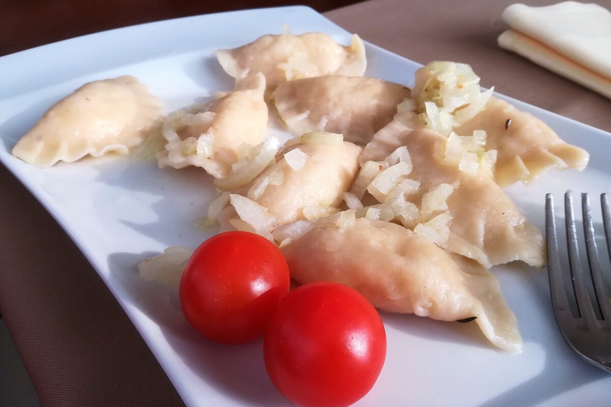 Pierogi ruskie polane szklistą cebulką na maśle, na białym talerzu z dwoma pomidorkami koktajlowymi